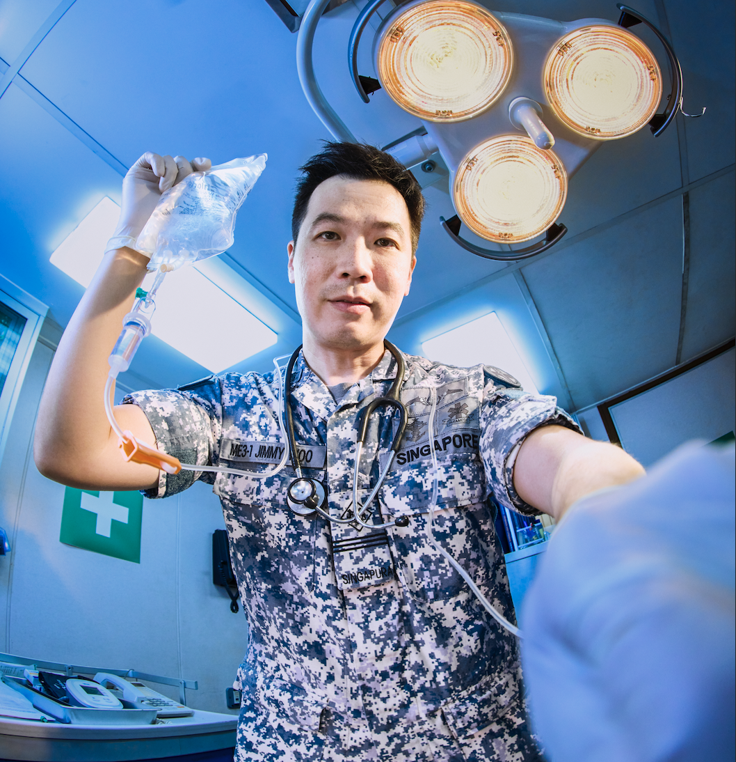 Navy medical expert is holding up an IV drip, and appears to be in the middle of a medical procedure